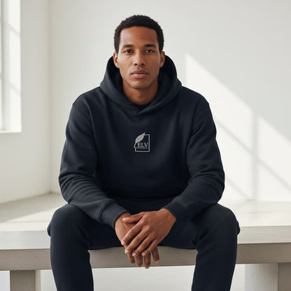 Man wearing a black hoodie with a logo sitting on a white bench in a bright room.