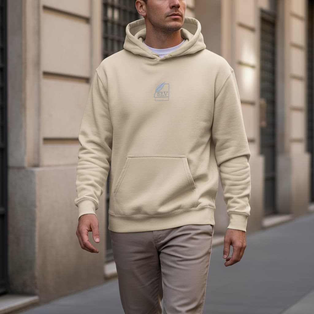 Man wearing a beige hoodie with a logo walking on a street.